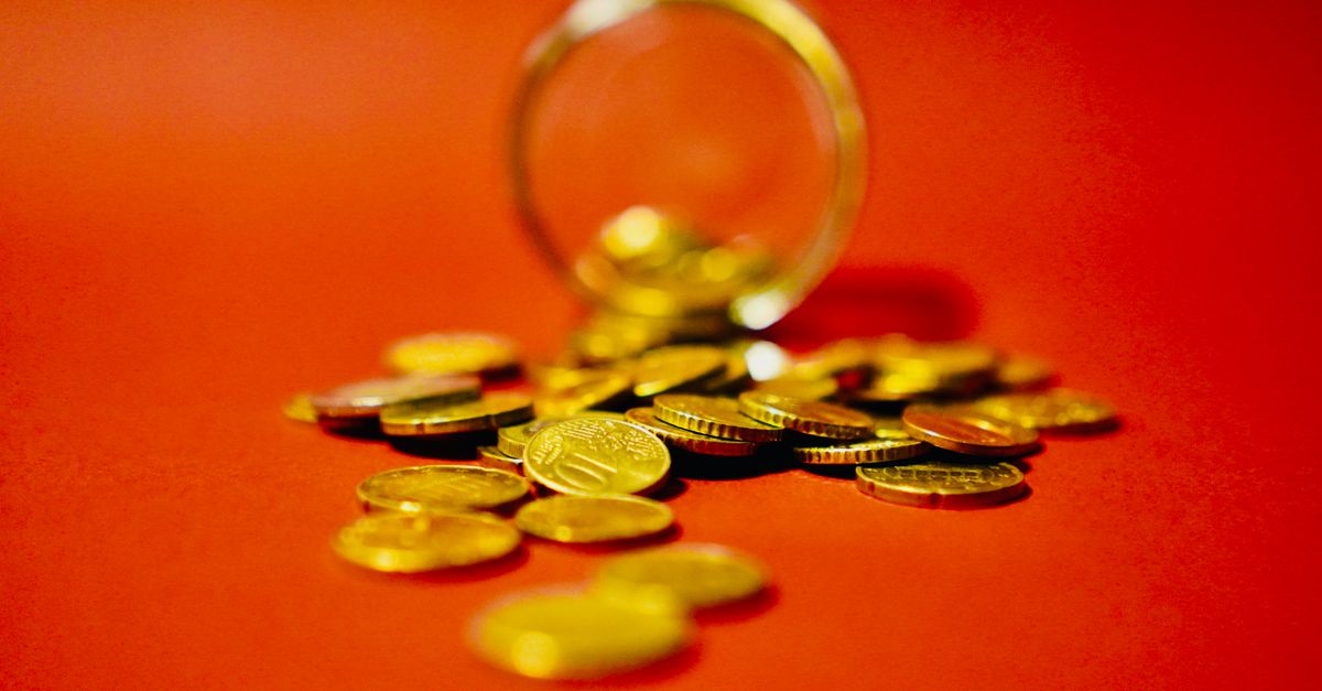 A collection of golden coins spilling from a glass jar on a vibrant red background symbolizes wealth.